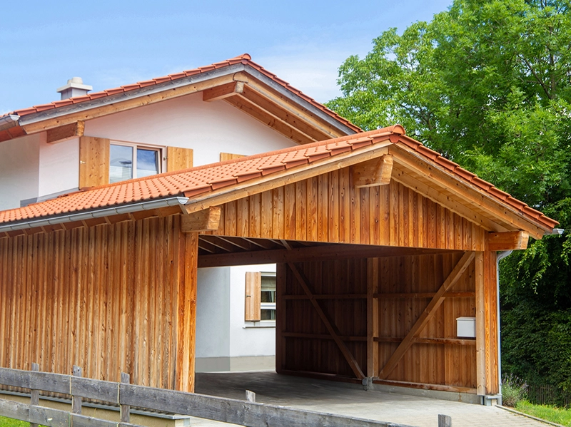 Überdachter Carport aus Holz vor einem Haus im alpinen Stil.